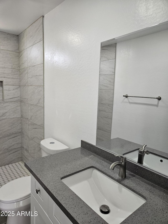 bathroom featuring tiled shower, vanity, and toilet