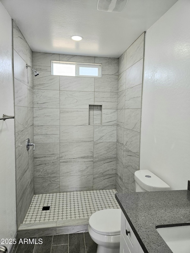 bathroom featuring vanity, tiled shower, and toilet