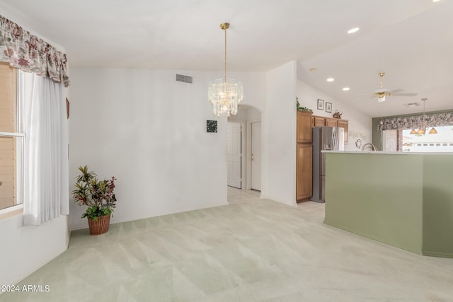 spare room featuring ceiling fan with notable chandelier, light carpet, and vaulted ceiling