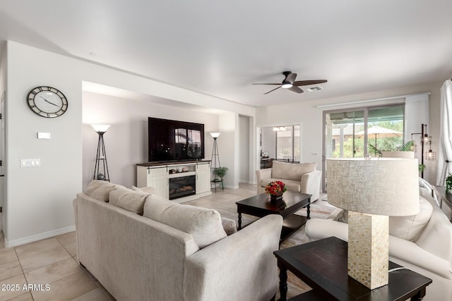 living room with light tile patterned flooring, ceiling fan, a glass covered fireplace, visible vents, and baseboards