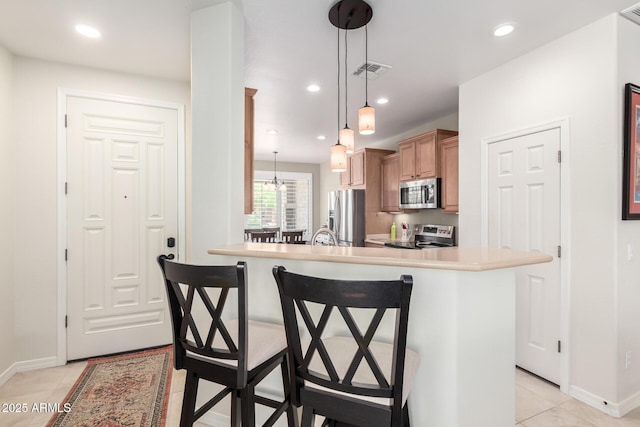 kitchen featuring light tile patterned floors, appliances with stainless steel finishes, visible vents, baseboards, and a kitchen bar