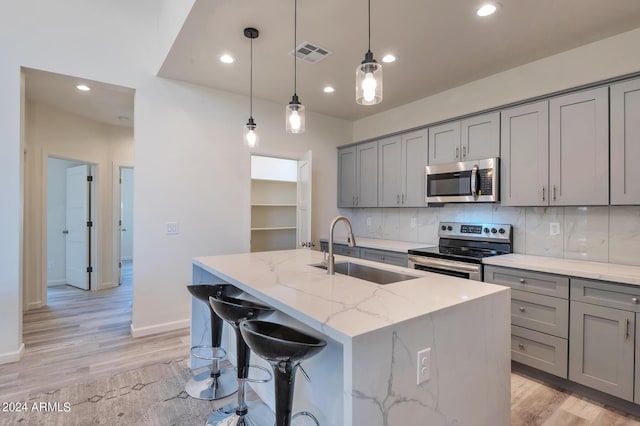 kitchen featuring appliances with stainless steel finishes, tasteful backsplash, sink, light stone counters, and a center island with sink