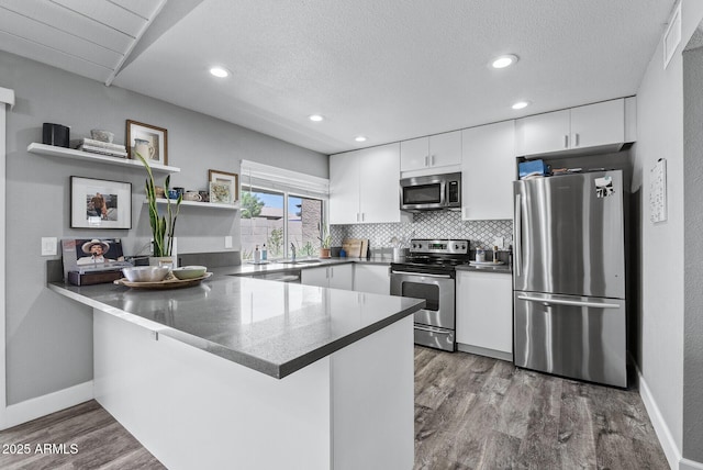 4502 W Continental Dr, Glendale, AZ 85308 - kitchen with stainless steel appliances, a peninsula, white cabinets, wood finished floors, and recessed lighting