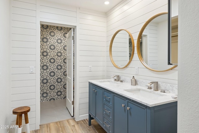 bathroom with double vanity, wood walls, a sink, and wood finished floors