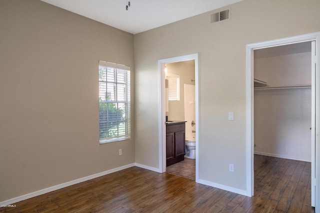 unfurnished bedroom with a walk in closet, connected bathroom, a closet, and dark hardwood / wood-style floors