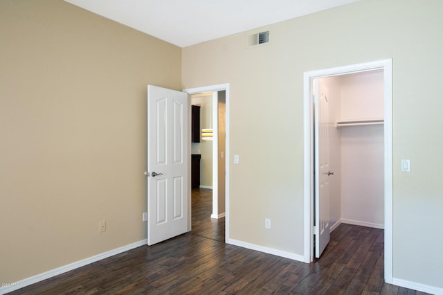 unfurnished bedroom featuring a walk in closet, dark hardwood / wood-style flooring, and a closet