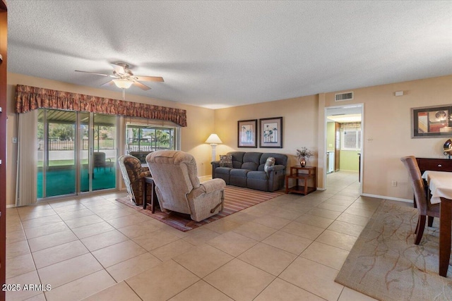 living area with ceiling fan, light tile patterned floors, a textured ceiling, visible vents, and baseboards