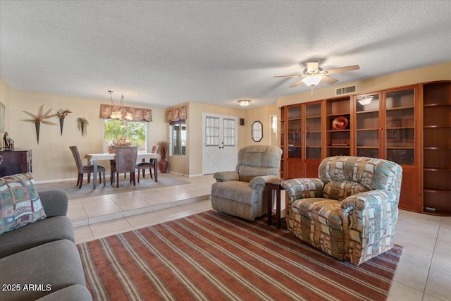 living room with a textured ceiling, ceiling fan with notable chandelier, light tile patterned floors, and visible vents