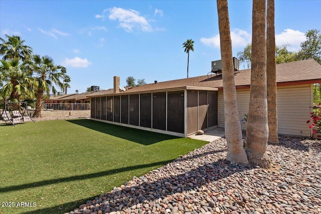 back of property featuring central AC, a sunroom, a yard, fence, and a shingled roof