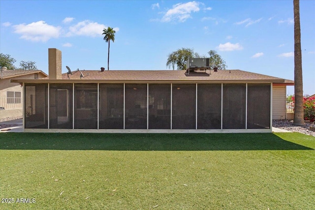 rear view of house with a sunroom, central AC, a chimney, and a lawn