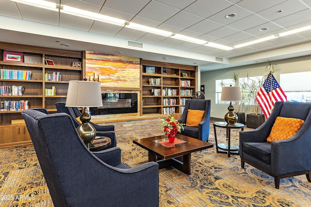 living area featuring visible vents, built in features, and a glass covered fireplace
