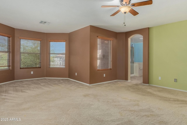 spare room featuring arched walkways, ceiling fan, visible vents, and light carpet
