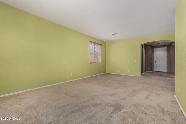 carpeted spare room with visible vents, arched walkways, and baseboards