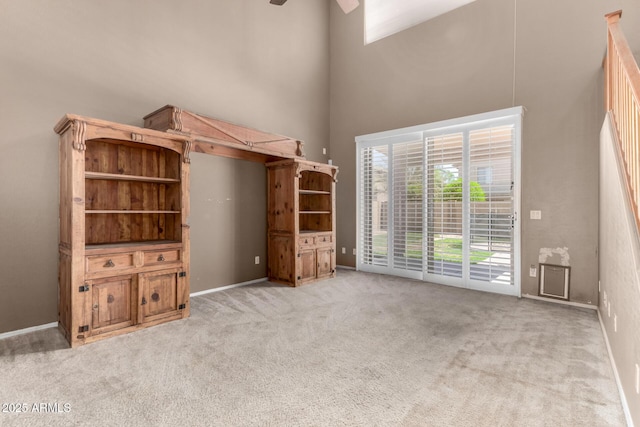 unfurnished living room with a ceiling fan, baseboards, light colored carpet, and a towering ceiling