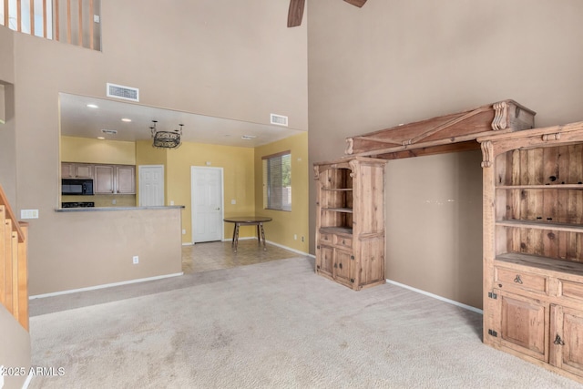 unfurnished living room with baseboards, a high ceiling, visible vents, and light colored carpet