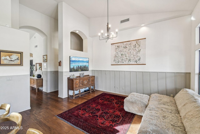 living area with visible vents, wainscoting, dark wood-style flooring, high vaulted ceiling, and a notable chandelier