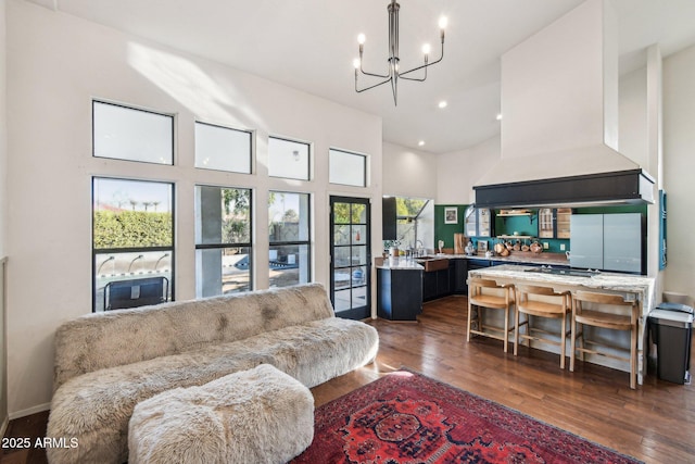 living room with dark wood-type flooring, a towering ceiling, sink, and a notable chandelier