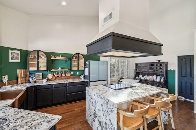 kitchen with light stone counters, a towering ceiling, fridge, and custom range hood