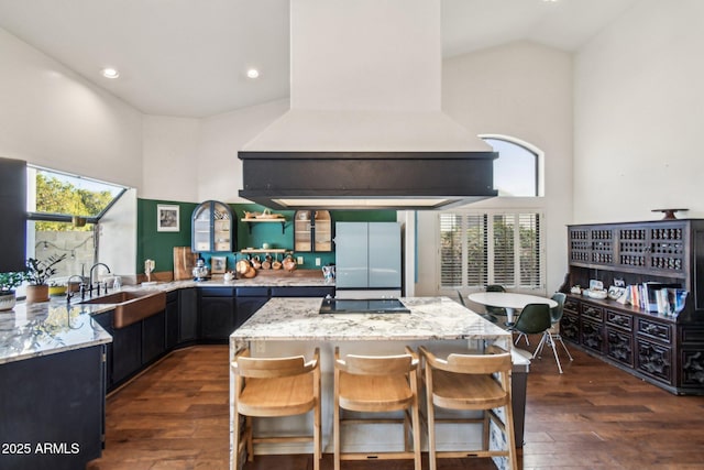 kitchen with a kitchen bar, custom exhaust hood, refrigerator, high vaulted ceiling, and light stone countertops