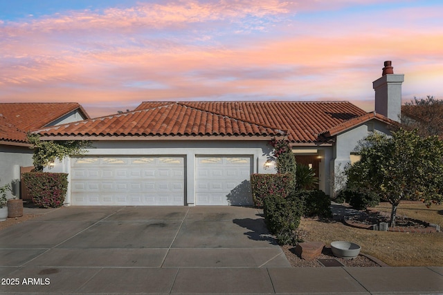 mediterranean / spanish house with a garage, driveway, a tile roof, and stucco siding