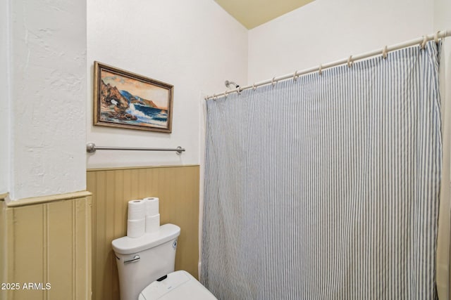 full bathroom featuring toilet, a shower with curtain, and wainscoting