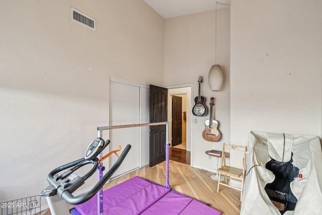 exercise room featuring a towering ceiling and light wood-type flooring