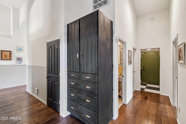 hallway featuring dark wood-type flooring, baseboards, visible vents, and a high ceiling