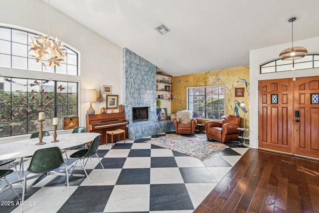 entryway with visible vents, a chandelier, wood finished floors, a stone fireplace, and high vaulted ceiling