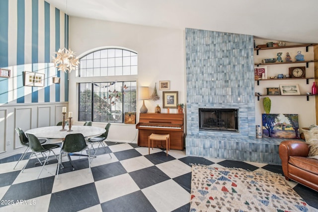 living room featuring a decorative wall, a tiled fireplace, wainscoting, vaulted ceiling, and tile patterned floors