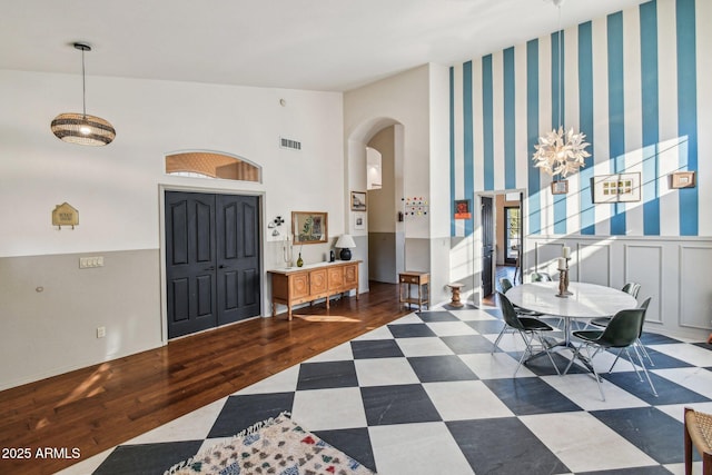 foyer featuring arched walkways, high vaulted ceiling, a wainscoted wall, dark wood-type flooring, and visible vents