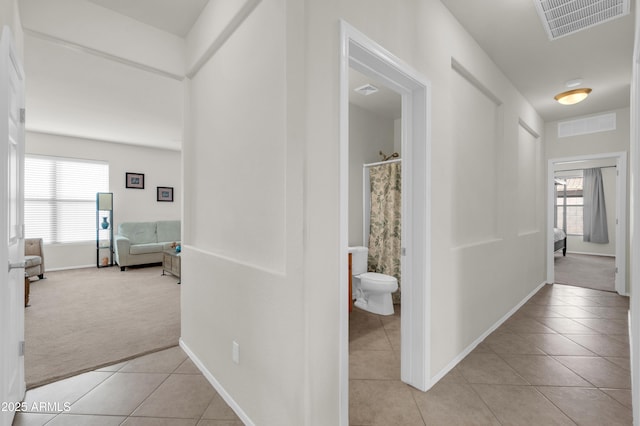 hall with a wealth of natural light, visible vents, light carpet, and light tile patterned flooring