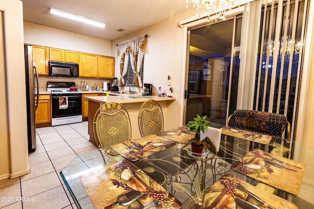 kitchen with light tile patterned floors, stainless steel fridge, a kitchen breakfast bar, gas stove, and kitchen peninsula