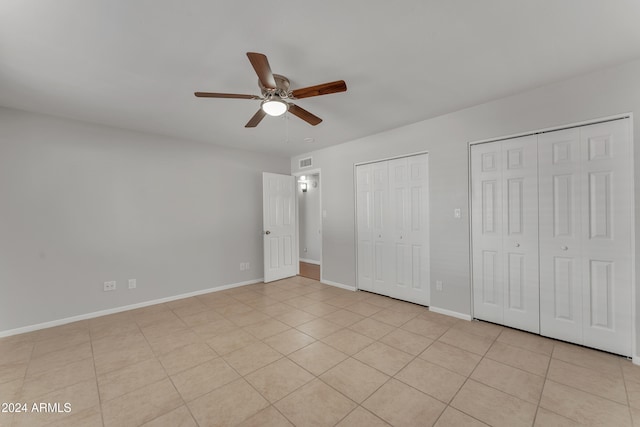 unfurnished bedroom featuring ceiling fan, light tile patterned floors, and two closets