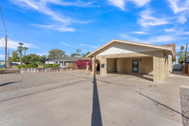 view of front facade with an attached carport, concrete driveway, fence, and brick siding