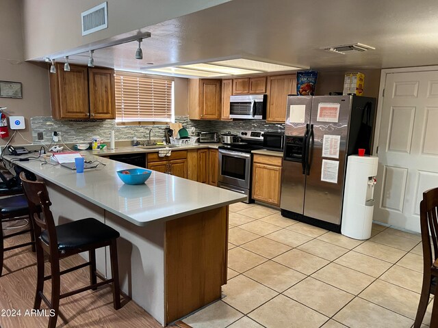 kitchen featuring appliances with stainless steel finishes, sink, kitchen peninsula, light tile patterned flooring, and a breakfast bar area