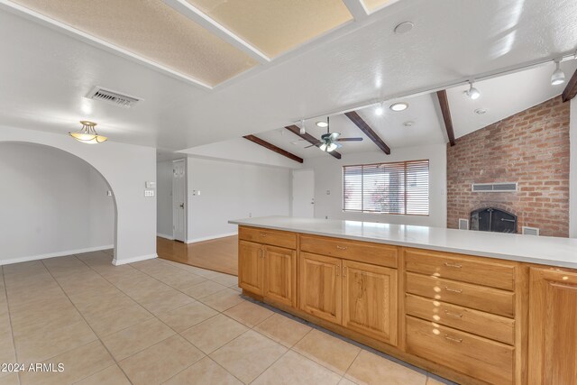 kitchen featuring light tile patterned flooring, ceiling fan, a fireplace, and lofted ceiling with beams