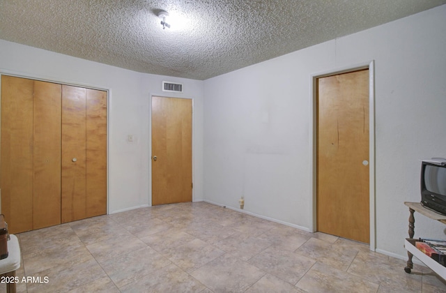 unfurnished bedroom with a textured ceiling, visible vents, and baseboards