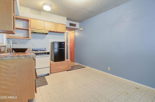 kitchen featuring a sink, under cabinet range hood, white gas range, visible vents, and freestanding refrigerator