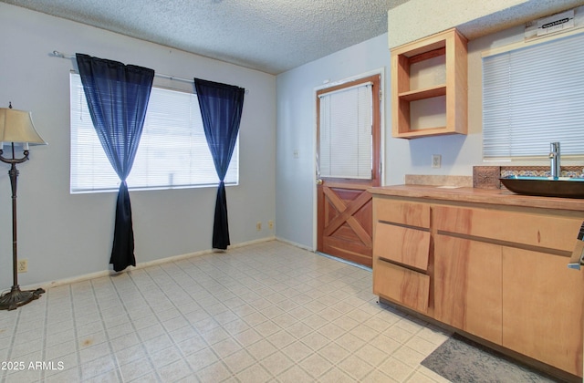 kitchen featuring open shelves, light countertops, a sink, baseboards, and a textured ceiling