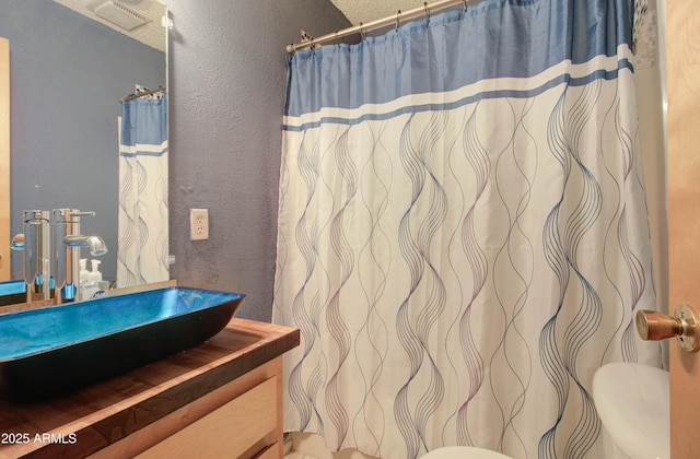 full bathroom featuring a shower with curtain, a textured wall, visible vents, toilet, and vanity