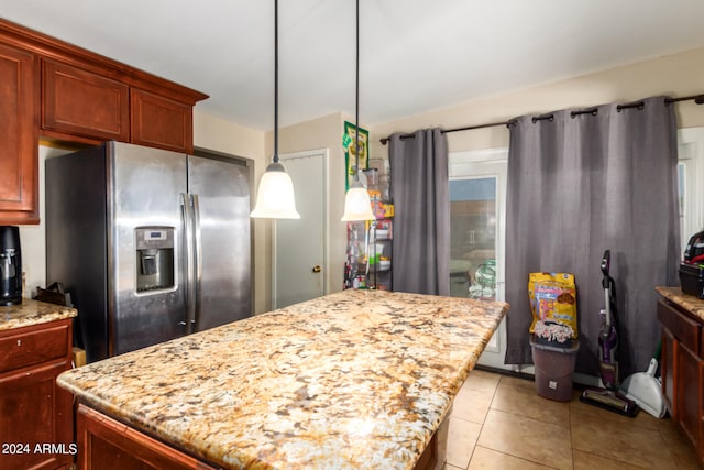 kitchen featuring light tile patterned floors, a kitchen island, stainless steel refrigerator with ice dispenser, light stone countertops, and decorative light fixtures