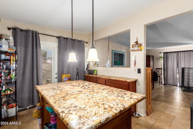 kitchen featuring pendant lighting, brown cabinetry, a kitchen island, and light stone countertops