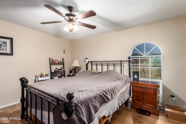 bedroom with a ceiling fan, a textured ceiling, baseboards, and wood finished floors