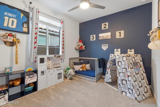 carpeted bedroom with a nursery area and a ceiling fan