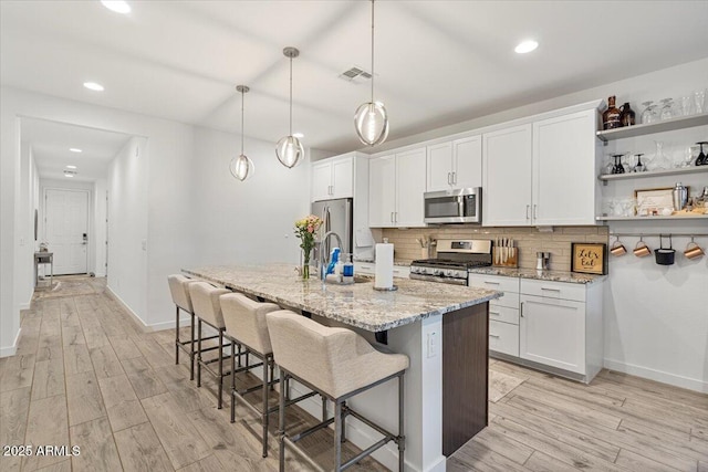 kitchen featuring light wood finished floors, decorative backsplash, appliances with stainless steel finishes, and a breakfast bar area