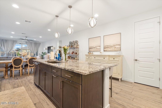 kitchen featuring stainless steel dishwasher, a sink, dark brown cabinetry, light wood-style flooring, and visible vents