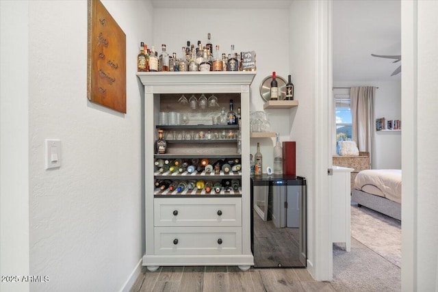 bar with a dry bar, baseboards, beverage cooler, and wood finished floors