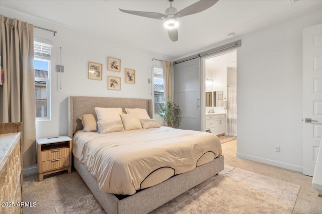 bedroom featuring light carpet, a barn door, ensuite bathroom, baseboards, and ceiling fan
