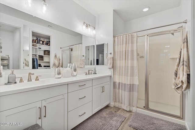 bathroom featuring a shower stall, wood finished floors, double vanity, and a sink