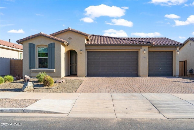 mediterranean / spanish house with a garage, a tiled roof, decorative driveway, and stucco siding